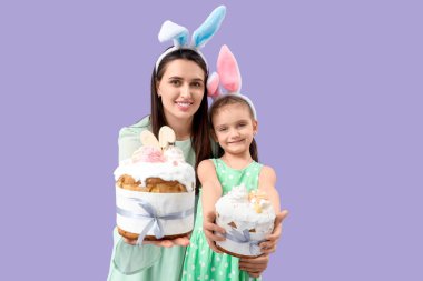 Güzel genç bir kadın ve küçük tatlı kızı tavşan kulaklı Paskalya pastaları ve leylak arkaplanlı