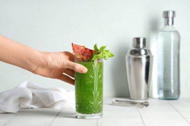 Beyaz arka planda pastırmalı ve kerevizli yeşil kanlı Mary kokteyli tutan kadın eli.