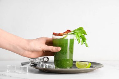 Beyaz arka planda pastırmalı ve kerevizli yeşil kanlı Mary kokteyli tutan kadın eli.