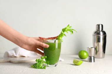 Beyaz arka planda pastırmalı ve kerevizli yeşil kanlı Mary kokteyli tutan kadın eli.