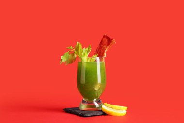 Kırmızı arka planda pastırmalı, kerevizli ve limonlu yeşil Bloody Mary kokteyli.
