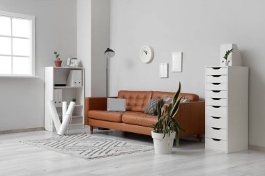 Modern dizüstü bilgisayarı ve yumuşak yastıkları olan kahverengi deri kanepe.