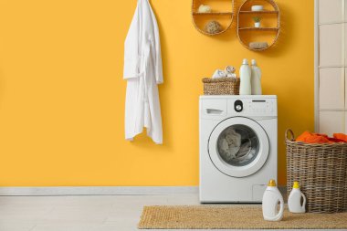 Modern çamaşır makinesi, hasır sepeti ve deterjan şişeleriyle şık bir çamaşır odası.