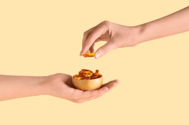 Renkli arka planda balık yağı kapsülleri olan kadın eller, yakın plan.