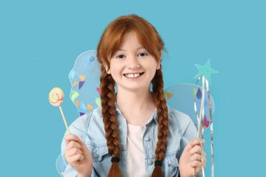 Peri kanatları ve mavi arka planda lolipopu olan tatlı kızıl saçlı kız.