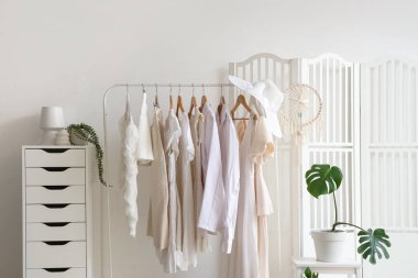 Giysi askılığı, katlama perdesi ve palmiye bitkisi olan butiğin içi.