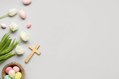 Lale çiçekli ahşap haç, gri arka planda yuva ve boyanmış yumurta. Paskalya kutlaması