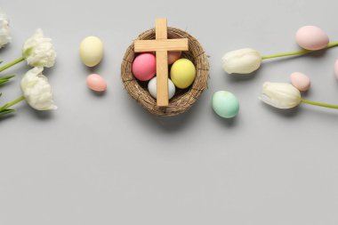 Lale çiçekli ahşap haç, gri arka planda yuva ve boyanmış yumurta. Paskalya kutlaması