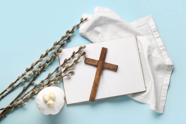 Söğüt dallı ahşap haç, Paskalya pastası ve mavi zemin üzerine boş kitap.