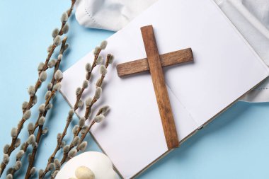 Söğüt dallı ahşap haç, Paskalya pastası ve mavi zemin üzerine boş kitap.