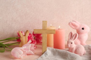 Çiçekli ahşap haç, yanan mumlar ve pembe grunge arka planda tavşanlar. Paskalya kutlaması