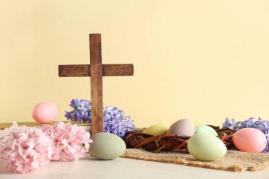 Ahşap haç, kitap, çiçekler ve beyaz masanın üzerine sarı grunge arka planına karşı boyanmış yumurtalar. Paskalya kutlaması