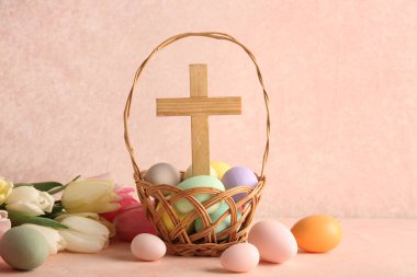 Ahşap haçlı hasır sepet, pembe grunge arka planda boyanmış yumurta ve lale çiçekleri. Paskalya kutlaması