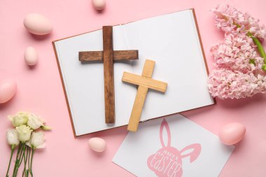 Ahşap haçlar, kitap, yumurta, çiçek ve pembe arka planda Mutlu Paskalyalar tebrik kartı.