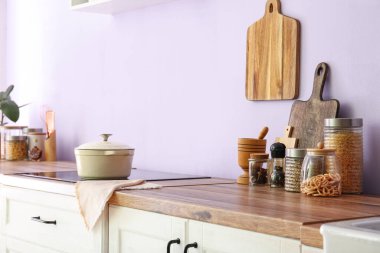 Mutfaktaki leylak duvarının yanındaki tezgahta tencere ve yemek kavanozlarıyla fırın.