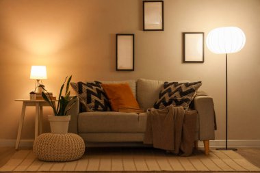 Modern oturma odasının içinde rahat bir kanepe, kabarık bir çiçek ve parlak lambalar.