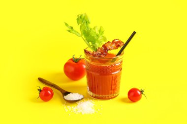Sarı arka planda domuz pastırması ve kereviz ile bir bardak Bloody Mary kokteyli.