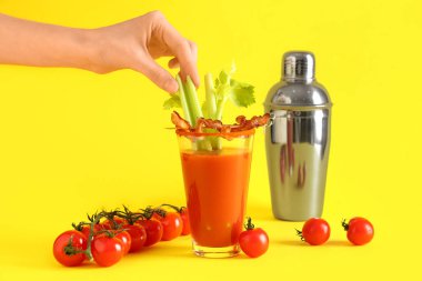 Kerevizli kadın eli ve sarı arka planda pastırmalı bir bardak Bloody Mary kokteyli.