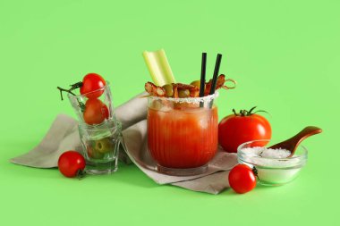 Yeşil arka planda domuz pastırması, zeytin ve kereviz ile bir bardak Bloody Mary kokteyli.