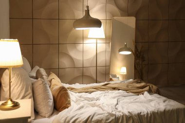 Geceleri rahat yatağı, aynası ve parlayan lambaları olan şık bir yatak odası.