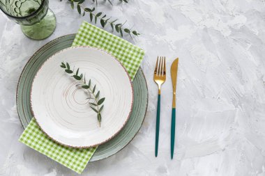 Altın çatal bıçak seti ve gri arka planda okaliptüs dalları olan güzel bir masa.