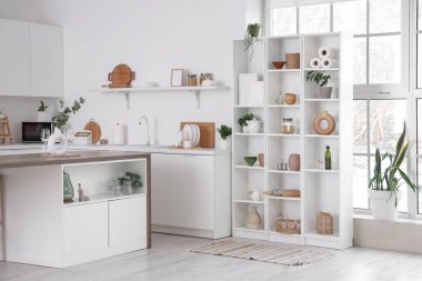 Beyaz tezgahlı, masa ve raf üniteli şık bir mutfak.