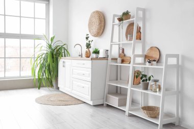 Beyaz tezgahlı, ev bitkisi ve raf üniteli şık bir mutfak.