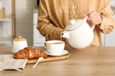 Ayçöreği olan kadın mutfakta fincana sıcak çay dolduruyor, yakın plan.