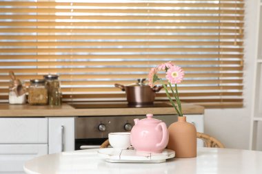 Pembe çaydanlık, bir fincan çay ve mutfaktaki masada güzel çiçekler.