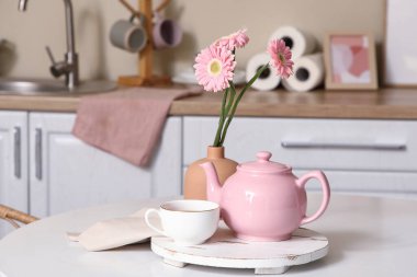 Pembe çaydanlık, bir fincan çay ve mutfaktaki masada güzel çiçekler.