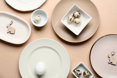 Farklı temiz tabaklar, bıldırcın yumurtaları ve bej arka planda tahta tavşanlar. Paskalya kutlaması