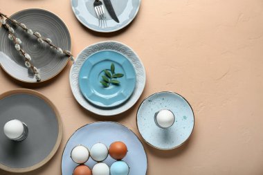 Different clean plates with Easter eggs, fresh leaves and pussy willow branches on beige background