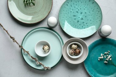 Different clean plates with Easter eggs, gypsophila flowers and pussy willow branch on grey background