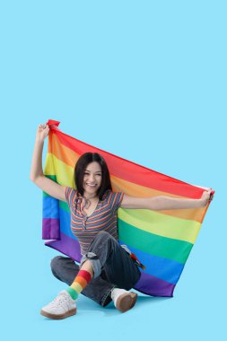 Gökkuşağı bayraklı güzel bir kadın mavi arka planda oturuyor. LGBT kavramı