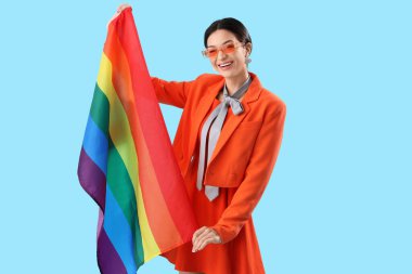 Mavi arka planda gökkuşağı bayrağı olan güzel genç bir kadın. LGBT kavramı