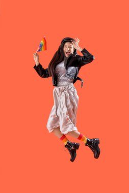 Turuncu arka planda gökkuşağı bayrağı atlayan güzel bir genç kadın. LGBT kavramı