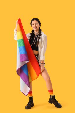Sarı arka planda gökkuşağı bayrağı olan güzel genç bir kadın. LGBT kavramı