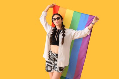 Sarı arka planda gökkuşağı bayrağı olan güzel genç bir kadın. LGBT kavramı
