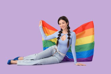 Gökkuşağı bayraklı güzel genç bir kadın leylak arka planda oturuyor. LGBT kavramı