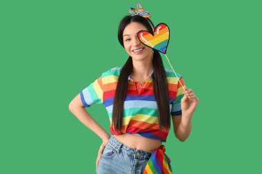 Gökkuşağı tişörtlü güzel bir kadın yeşil arka planda gururlu bir kalp taşıyor. LGBT kavramı