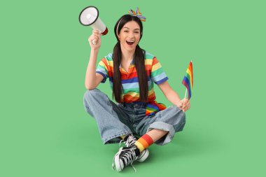 Gökkuşağı tişörtlü güzel bir kadın elinde gurur bayrağı ve yeşil arka planda hoparlör tutuyor. LGBT kavramı