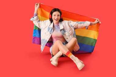 Kırmızı arka planda gökkuşağı bayrağı olan güzel genç bir kadın oturuyor. LGBT kavramı