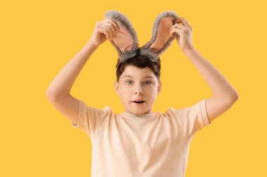 Sarı arka planda tavşan kulaklı, şaşırmış genç bir çocuk. Paskalya kutlaması