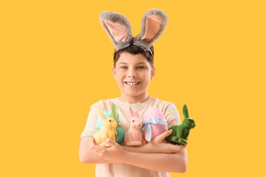 Tavşan kulaklı, paskalya tavşanları ve sarı arka planda yumurtaları olan genç bir çocuk.