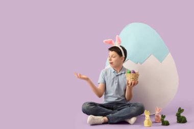 Paskalya yumurtası ve tavşanlarıyla tavşan kulaklı genç çocuk leylak arka planda bir şeyler gösteriyor.