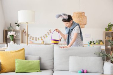 Evde paskalya yumurtası arayan tavşan kulaklı genç bir çocuk.