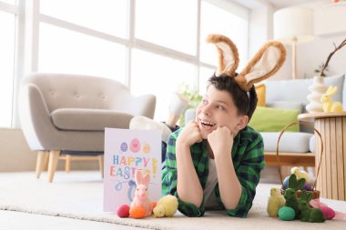 Tavşan kulaklı, paskalya dekoru olan, evde yerde yatan genç bir çocuk.