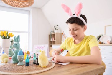 Mutfaktaki masada tavşan kulaklı genç çocuk resim çiziyor.