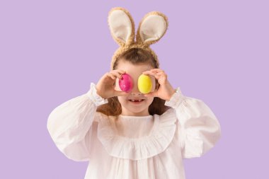 Leylak arka planında Paskalya yumurtaları olan tavşan kulaklı şirin bir kız.