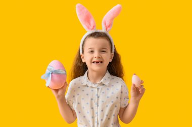 Sarı arka planda Paskalya yumurtaları olan tavşan kulaklı şirin bir kız.